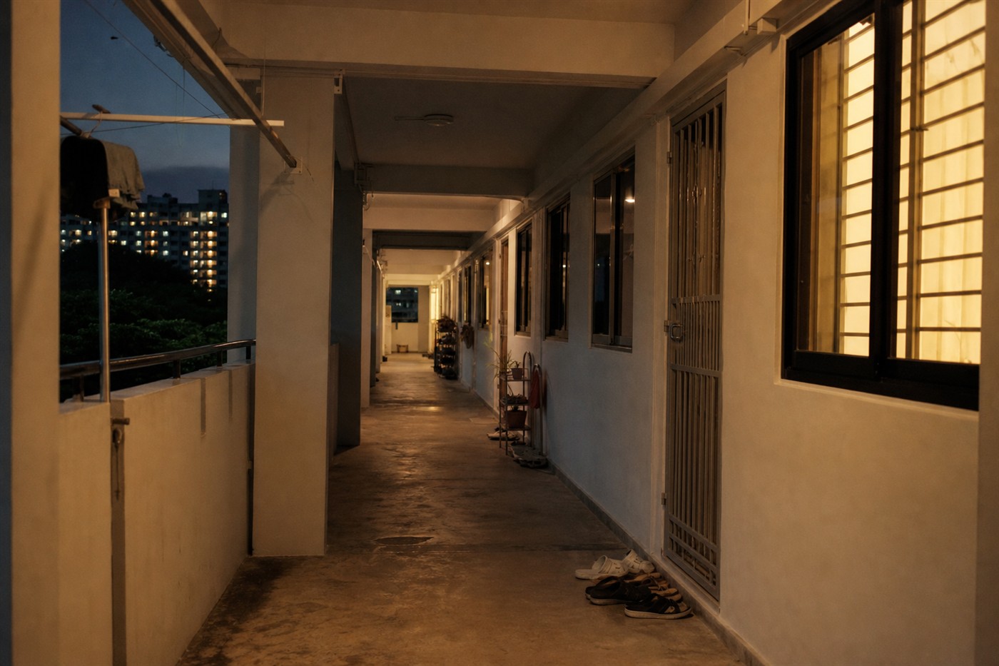 HDB corridor at dusk with shoes by the door and warm light from a window